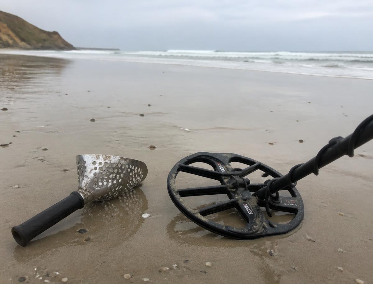 Metal detector coil and sand scoop resting on wet sand at the beach in the morning
